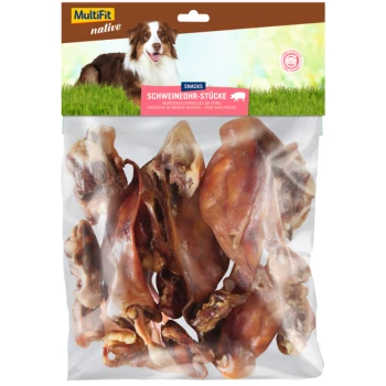 Eine durchsichtige Tüte mit "MultiFit native Snacks" Schweineohrstücken mit dem Etikett "SCHWEINEOHR-STÜCKE" und einem braun-weißen Hund im Hintergrund.