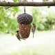 Zwei kleine Vögel sitzen auf einem einzigartigen, eichelförmigen Vogelhaus, das mit Samen gefüllt ist, und hängen von einem Baumzweig in einer grünen Umgebung.