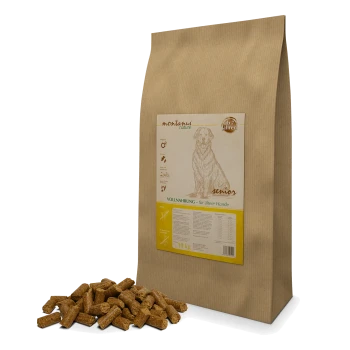 Braune Papiertüte mit Hundefutter, beschriftet mit "montanus' nature senior" für ältere Hunde, mit Futterstücken, die davor verstreut sind.
