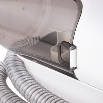 Nahaufnahme eines Haustierpflegegeräts mit einer transparenten Abdeckung, einem grauen flexiblen Schlauch und einem sicheren Verriegelungsmechanismus.