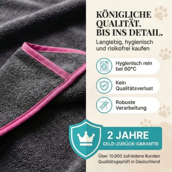 Eine Person wickelt einen glücklichen Hund in ein dunkelgraues Handtuch mit pinkem Rand auf grünem Gras. Der Text lautet "DAS SUPER SAUGSTARK WOHLFÜHLTUCH."
