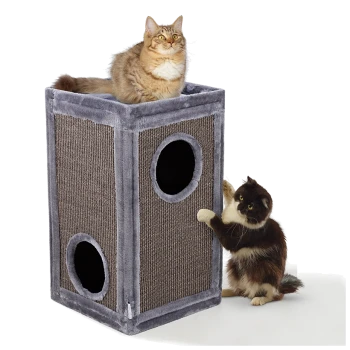 Eine flauschige braune getigerte Katze sitzt auf einem grau-braunen Katzenhaus, während eine schwarz-weiße Katze spielerisch an einem Seiteneingang kratzt.