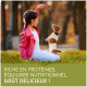 Un enfant en veste rose est assis sur l'herbe, tenant une friandise pour un chiot excité. Texte : "Riche en protéines, équilibre nutritionnel, goût délicieux !"