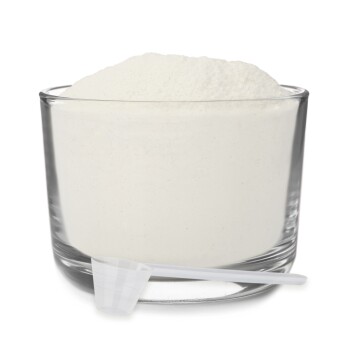 Eine klare Glasschüssel gefüllt mit weißem Pulver, begleitet von einem kleinen weißen Messlöffel, der daneben liegt.