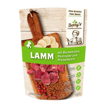 Glücklicher hellfarbener Welpe läuft auf Gras neben Betty's Landhausküche Hundefutterpaketen mit dem Text „Für echte Feinschmecker“.