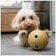 Een pluizige, lichtgekleurde hond speelt met een KONG-speelgoed op een betegelde keukenvloer, met traktaties verspreid in de buurt.