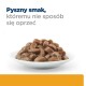 Biała miska wypełniona wilgotną, kawałkową karmą dla zwierząt, o bogatym brązowym kolorze. Tekst brzmi: "Pyszny smak, któremu nie sposób się oprzeć."