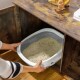 Eine Person hält eine grau-weiße Katzenstreu-Box, die mit Streu gefüllt ist, positioniert in einem Holzschrank.