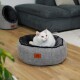 Ein gemütliches graues Haustierbett mit schwarzem Innenraum, das ein Lederetikett hat, steht auf einem Holzboden. Eine weiße Katze hat sich bequem im Bett zusammengekuschelt.