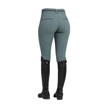 Eine Frau trägt eng anliegende tealfarbene Reithosen mit einem strukturierten Griffmuster auf dem Gesäß, kombiniert mit hohen schwarzen Reitstiefeln.