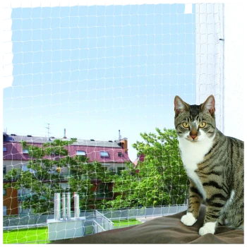 Un chat tigré est assis sur un coussin marron devant une fenêtre avec un filet de sécurité, surplombant une zone extérieure verte et des bâtiments.