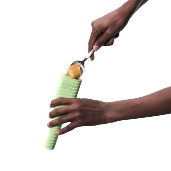 Une personne utilisant une cuillère pour remplir un distributeur de friandises en silicone vert avec du beurre de cacahuète, conçu pour les friandises pour animaux.