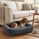 Beagle liegt auf einem grauen, gerippten Plüschhundebett in einem gemütlichen Wohnzimmer neben einem beigen Sofa und einem Holzcouchtisch mit einer Tasse.