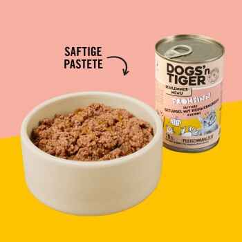 Schüssel mit stückigem Tierfutter neben einer Dose mit der Aufschrift "DOGS'n TIGER Schlemmer-Menü Frohsinn" mit Hühnerherzen und Kürbis.