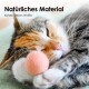 Eine verspielte getigerte Katze schlägt nach bunten Filzkugeln auf einem Holzboden, mit pinken, blauen, grünen und lila Kugeln, die verstreut sind.