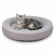 Grau getigerte Katze mit grünen Augen liegt in einem runden hellgrauen Plüsch-Tierbett mit erhöhtem Rand.