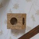 Geflochtener Strohwürfel für Haustiere mit zwei runden Öffnungen, an einer Wand mit floralem Tapetenhintergrund montiert.