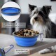 Eine blaue zusammenklappbare Haustierschüssel, die mit Hundefutter gefüllt ist, mit einem Karabiner für eine einfache Befestigung. Ein Hund ist im Hintergrund sichtbar.
