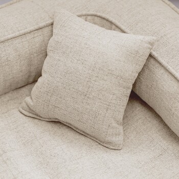 Ein flauschiger grauer Hund, der auf einem stilvollen beigen Haustierbett liegt, mit einem kleinen Busch im Hintergrund und einer modernen Gebäudefassade.