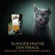 Eine graue Katze, die sich die Lippen leckt, neben einem Sheba Nature's Collection Futterbeutel, mit dem Text 'mit Truthahn' und 'AUSGEZEICHNETER GESCHMACK'.