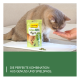 Graue Katze schnuppert an einer Hand neben einer GimCat GrasBits-Tüte und -Pellets; sichtbarer Text: 'DIE PERFEKTE KOMBINATION AUS GENUSS...'.