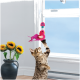 Chat tigré debout sur les pattes arrière, atteignant un jouet oiseau rose à plumes suspendu près d'une fenêtre ensoleillée ; vase de tournesols