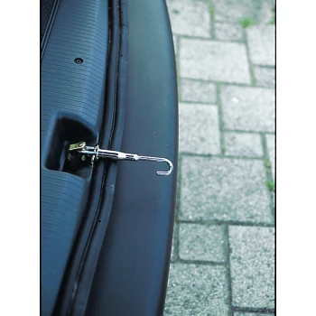 Auto Heckbelüfter Airboy Bild eines silbernen Hakens, der an einer schwarzen Oberfläche, möglicherweise einem Kofferraum, mit einem strukturierten Hintergrund aus Steinpflaster befestigt ist.