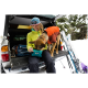 Eine Person in einer gelben Jacke sitzt auf einem Truck und füttert einen braunen Hund in einem orangefarbenen Mantel aus einem blauen Sack, mit schneebedeckten Bäumen im Hintergrund.