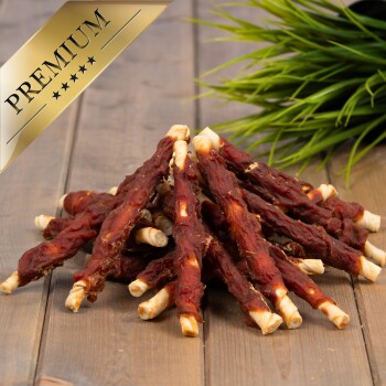 Ein Haufen hochwertiger Hundeleckerlis aus gedrehten Fleischstangen, auf einer Holzoberfläche mit grünem Gras im Hintergrund präsentiert.