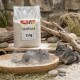 Ein graues Chinchilla sitzt neben einem Sack Chinchillasand mit der Aufschrift 'PANTO', vor einem leuchtend gelben Hintergrund. Der Sack wiegt 25 kg.