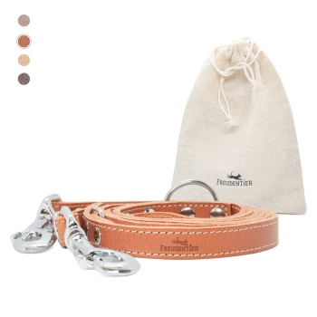 Eine tanfarbene Lederleine für Hunde mit silbernen Metallclips, ordentlich neben einem kleinen beigen Beutel mit Kordelzug, der das Logo 'Freudentier' trägt.