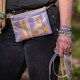 Taillenaufnahme: pastellfarbene, geometrische Hüfttasche mit gelbem Logoschild; Hand hält mehrere Leinen und Perlenarmbänder.