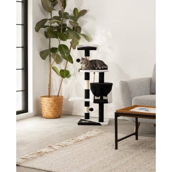 Ein gemütliches Wohnzimmer mit einem schwarz-weißen Katzenbaum, auf dem eine graue Katze auf der obersten Plattform entspannt, einem Topfpflanze und einem grauen Sofa.
