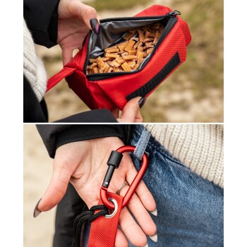 Eine Person, die eine rote Leckerlitasche für Haustiere hält, gefüllt mit braunen Leckerlis, mit einem Karabiner, der an ihrer Jeans befestigt ist.