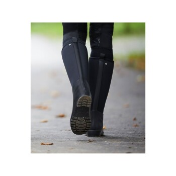 Eine Person, die auf einem Weg mit schwarzen Gummistiefeln geht, mit Fokus auf die Stiefel und ihr Profil.