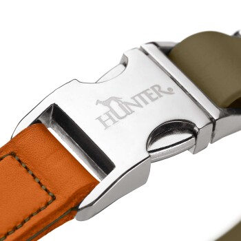 Nahaufnahme einer chromfarbenen Halsbandschnalle mit Gravur „HUNTER“, an einem orange abgesteppten Lederband und einem olivfarbenen Riemen.