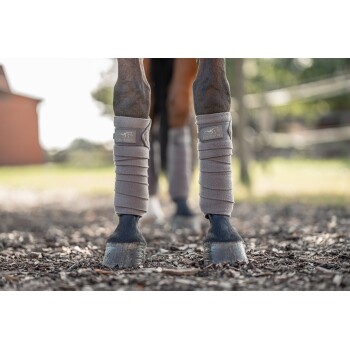 Zwei Pferdebeine, die in hellbeigen Schutzwickeln eingewickelt sind, mit dem sichtbaren Logo "EQUINATE", stehen auf einem strukturierten Boden.