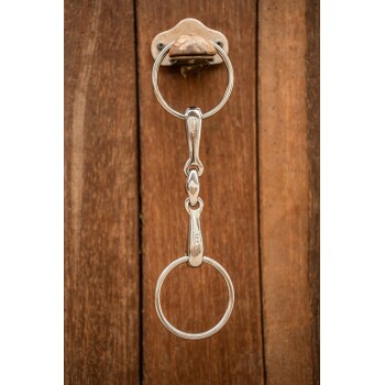 Eine Nahaufnahme eines glänzenden silbernen Schlüsselanhängers in Form eines Pferdegebisses, das auf einer Holzoberfläche hängt.