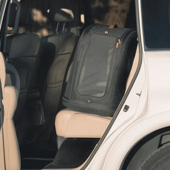 Eine schwarze Haustiertrage mit Netzpaneelen steht auf dem beigen Sitz eines Autos und zeigt ihr geräumiges Design für reisende Haustiere.