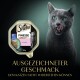 Eine graue Katze leckt sich die Lippen neben einer Sheba Finesse Katzenfutterpackung, die "mit Lachs" und den Text "AUSGEZEICHNETER GESCHMACK" zeigt.