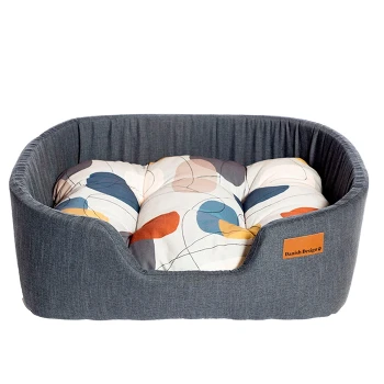 Ein gemütliches Haustierbett mit einem dunkelgrauen Stoffbezug und einem bunten, gemusterten Kissen mit abstrakten Formen in sanften Farben.