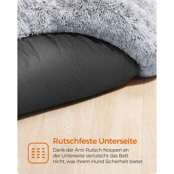 Nahaufnahme eines grauen Plüsch-Hundebetts mit punktierter, rutschfester schwarzer Unterseite auf Holzfußboden; sichtbarer Text 'Rutschfeste Unterseite'.