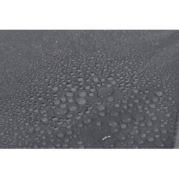 Nahaufnahme einer strukturierten grauen Oberfläche, die mit zahlreichen Wassertropfen bedeckt ist und ihre wasserdichte Qualität zeigt.