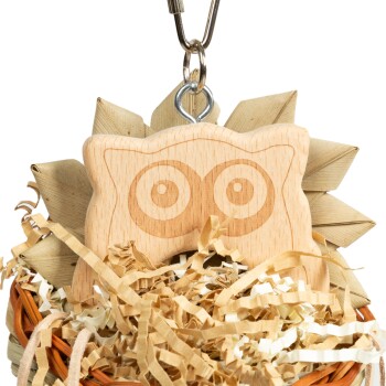 Holzspielzeug in Form einer Eule, eingebettet in zerknülltem Papier in einem geflochtenen Korb, mit großen, ausdrucksvollen Augen.