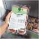 Hand hält eine gefrorene BARFER'S Komplett‑Mix Rind & Geflügel Katzenfutter‑Packung (400 g) im Gefrierschrank, mit sichtbaren Fleischstücken.