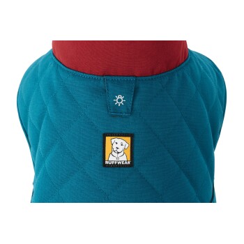 Eine Nahaufnahme einer türkisfarbenen Hundejacke mit rotem Kragen, die ein schwarzes und gelbes "Ruffwear"-Logo zeigt, das einen Hund darstellt.