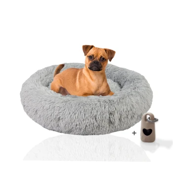 ® Hundebett Donut mit Gratis-Beigabe, Extra flauschiges Hundekissen M Ein kleiner Hund sitzt bequem in einem flauschigen grauen Haustierbett, neben einem beigen Haustierzubehör mit einem herzförmigen Ausschnitt.