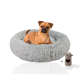 Ein kleiner Hund sitzt bequem in einem flauschigen grauen Haustierbett, neben einem beigen Haustierzubehör mit einem herzförmigen Ausschnitt.