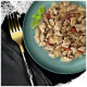 Gros plan d'une assiette de nourriture pour animaux de compagnie avec de la viande effilochée mélangée à des légumes, garnie d'une feuille de basilic, à côté d'une fourchette dorée sur une serviette sombre.