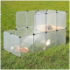 Ein transparenter Meerschweinchenkäfig auf Gras, mit einer Rampe, Holzstämmen und einem kleinen Versteck, mit zwei sichtbaren Meerschweinchen darin.